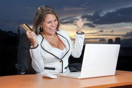 A happy woman in front of her laptop with a credit card in one hand.