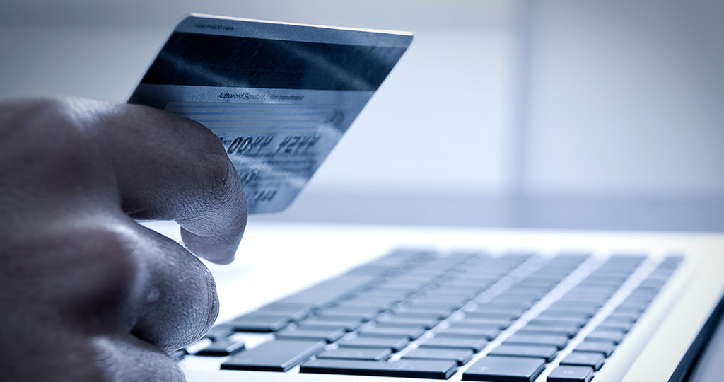 A man holding a credit card by a laptop