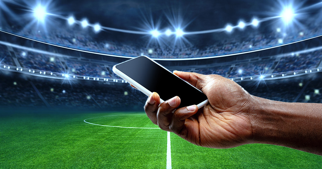 Hands holding smartphone in front of a sports game 