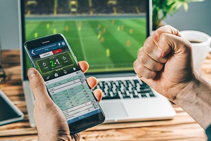 A man betting on his mobile in front of a desktop screen