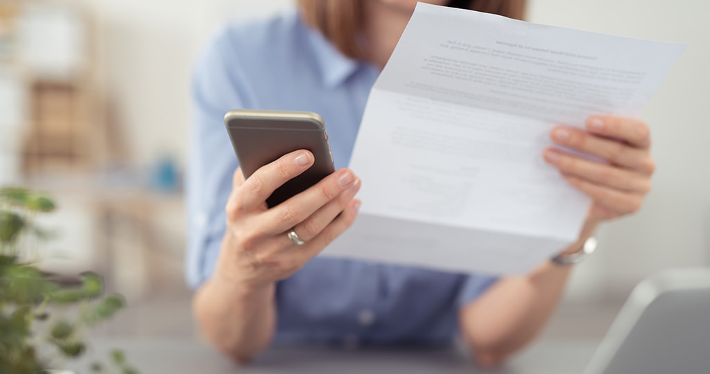 Person holding a mobile phone by a business paper 