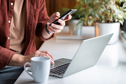 A man holding a smartphone in front of a laptop screen