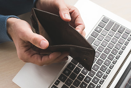 A hand holding an empty wallet by a laptop keyboard