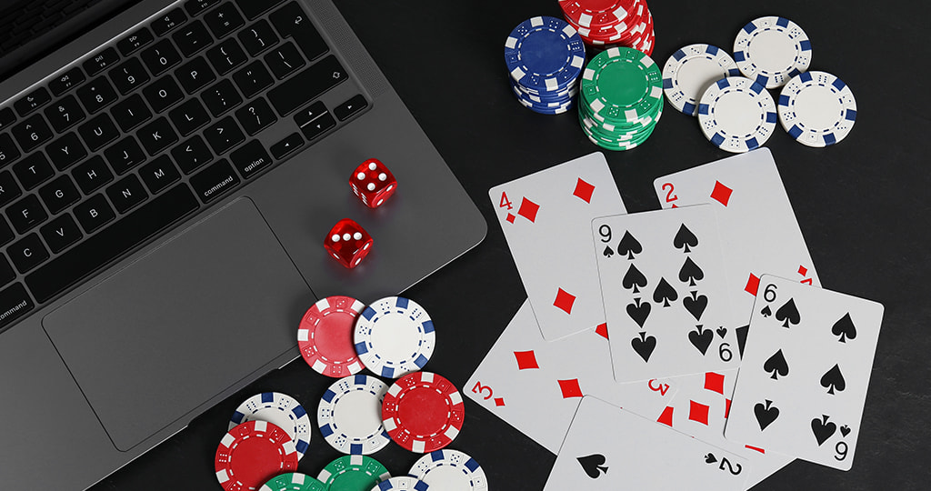 A laptop surrounded by poker chips and playing cards